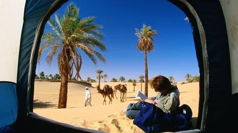 Tourist outside tent with bedouin and camels in background. Lonely Planet Images.