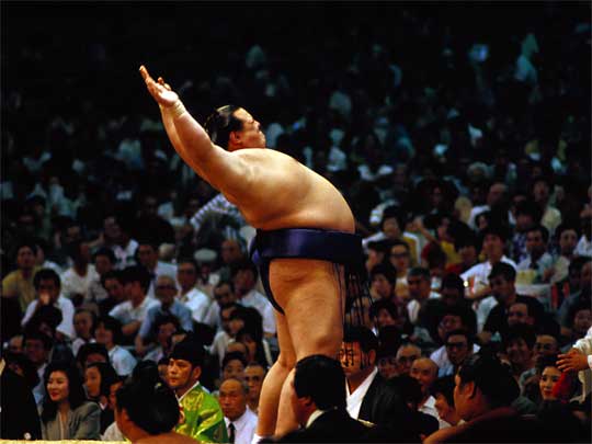 A Sumo wrestler performs his pre-bout stretching at a packed stadium